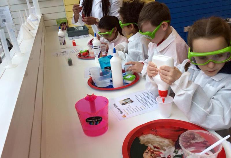 Kids with lab coats and goggles making experiments and the teacher helping them